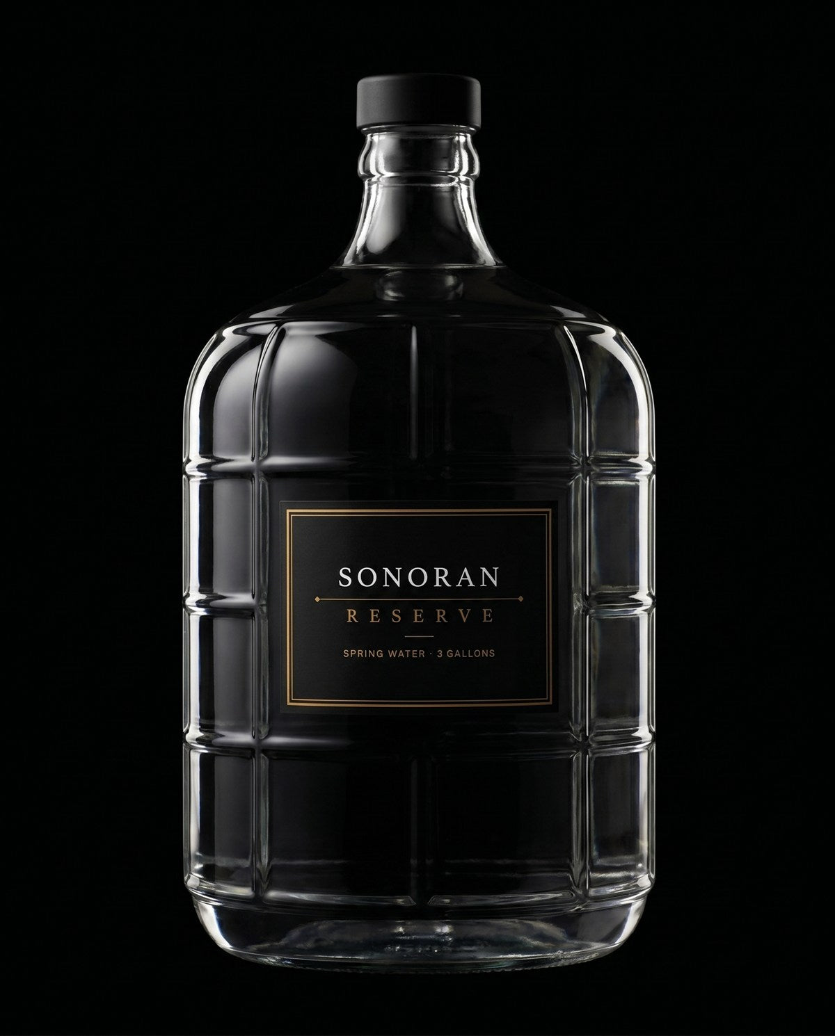 The Sonoran Reserve 3-gallon Italian glass carboy lit against pure black, its gold label reading Sonoran Reserve, Spring Water, 3 Gallons.